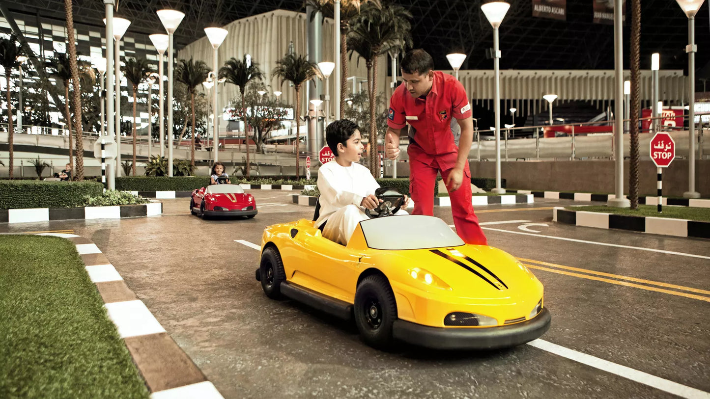 Two people with a yellow toy car on a road with palm trees and buildings in the background.