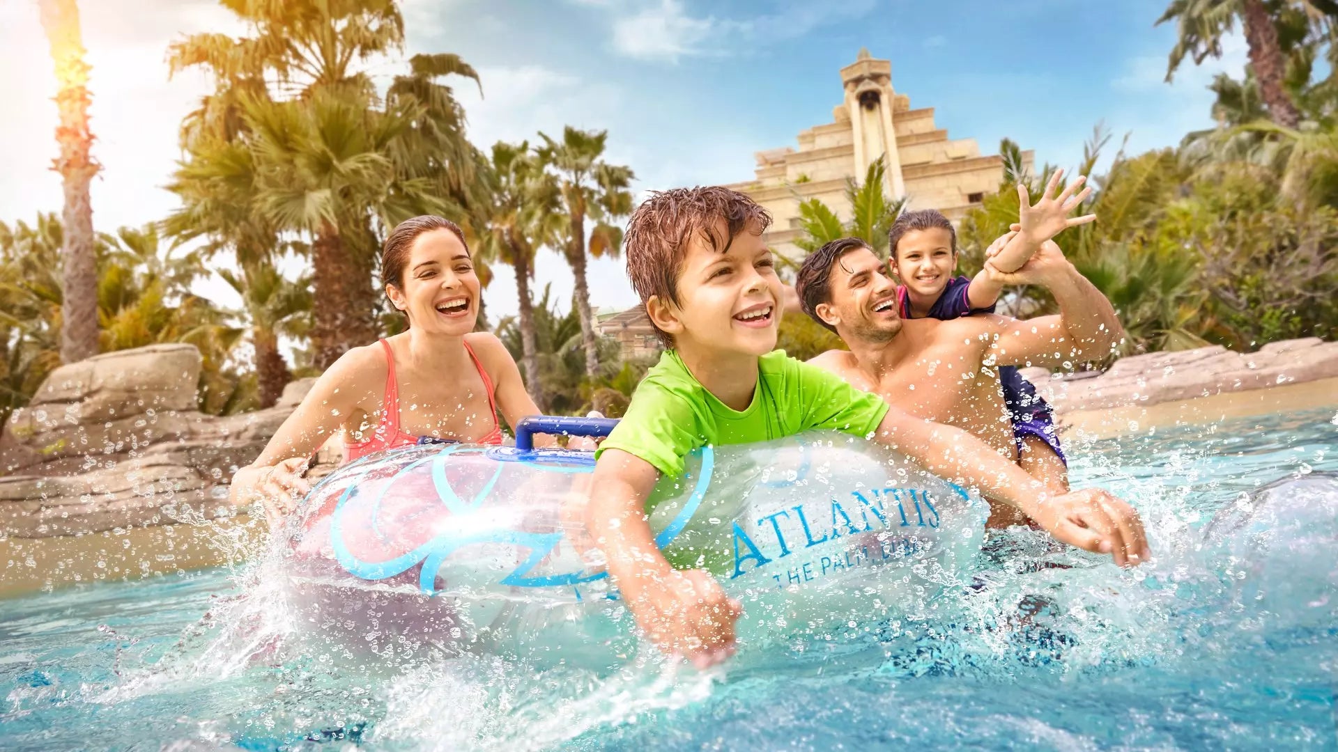 Family enjoying a water ride at Atlantis, The Palm with palm trees and a building in the background.