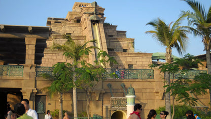 Architectural structure with a water slide, surrounded by palm trees and people.
