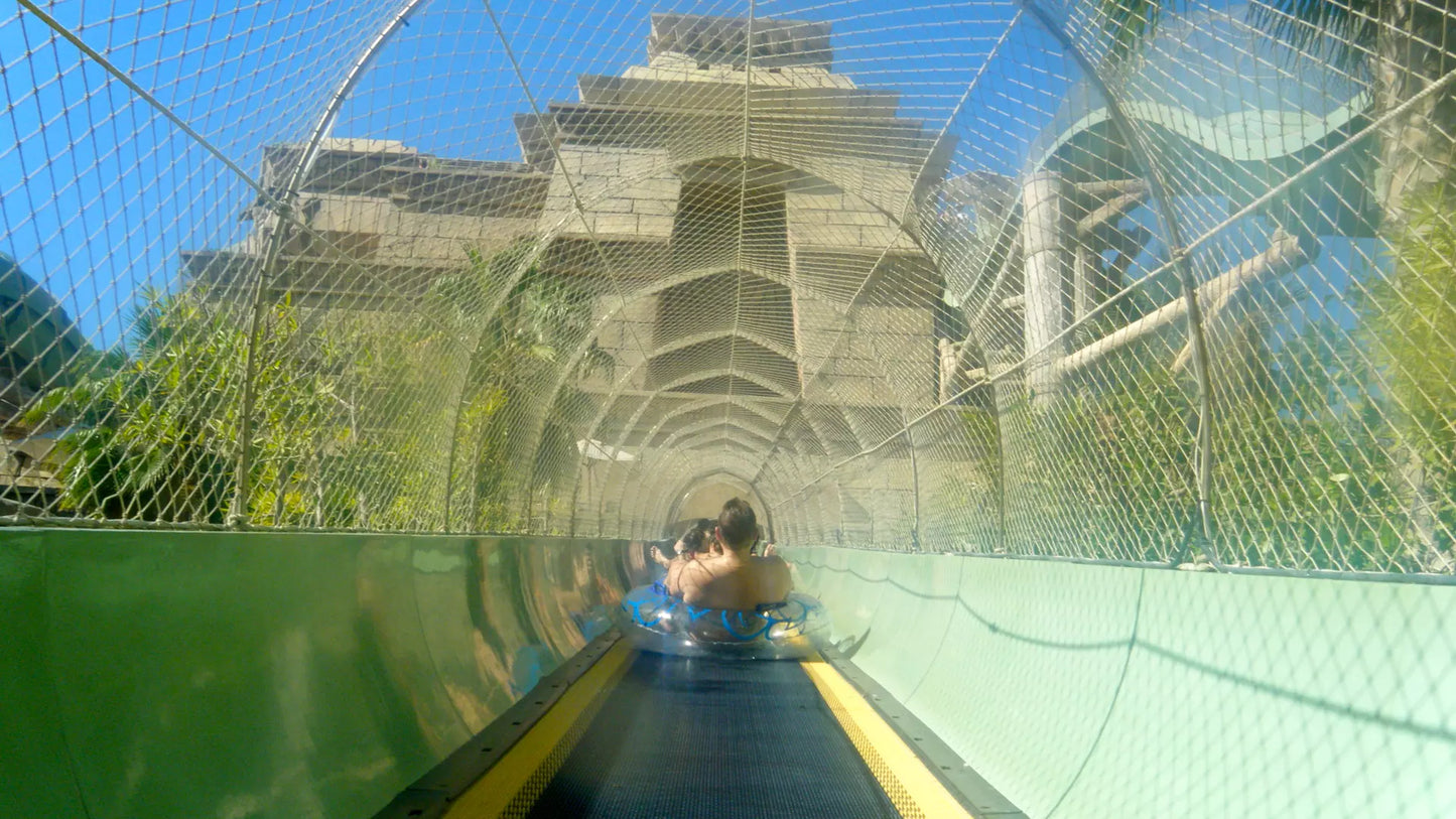 Person sliding down a water slide with a netted safety barrier at an amusement park.