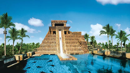 Stylized pyramid structure with water feature surrounded by palm trees under a blue sky.