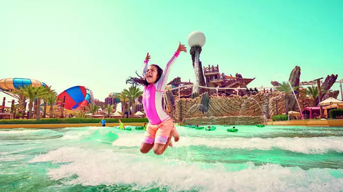 Person playing in a water park with a colorful slide and palm trees in the background
