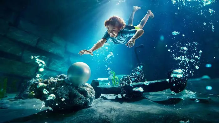 Person swimming underwater with a scooter, surrounded by marine life.
