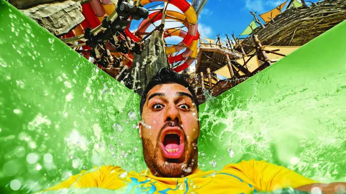 Person with a surprised expression in a water park with colorful slides and structures.