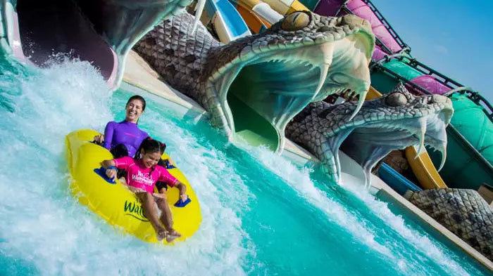 Two people on a yellow inner tube at a water park with a large dragon-like structure.