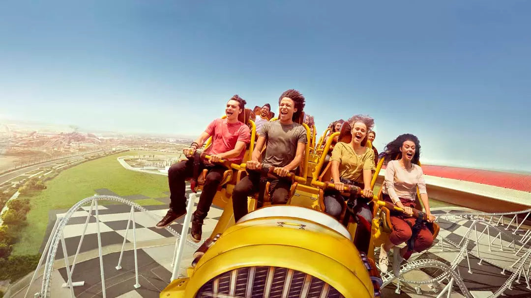 People enjoying a roller coaster ride with a clear blue sky and green landscape in the background.