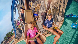 People on a roller coaster with a pool area in the background