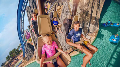 People on a roller coaster with a pool area in the background