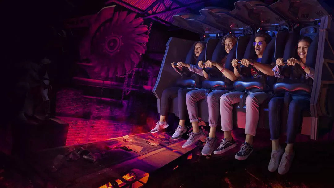Group of people on a dark, futuristic roller coaster ride with glowing red lights.