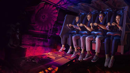 Group of people on a dark, futuristic roller coaster ride with glowing red lights.