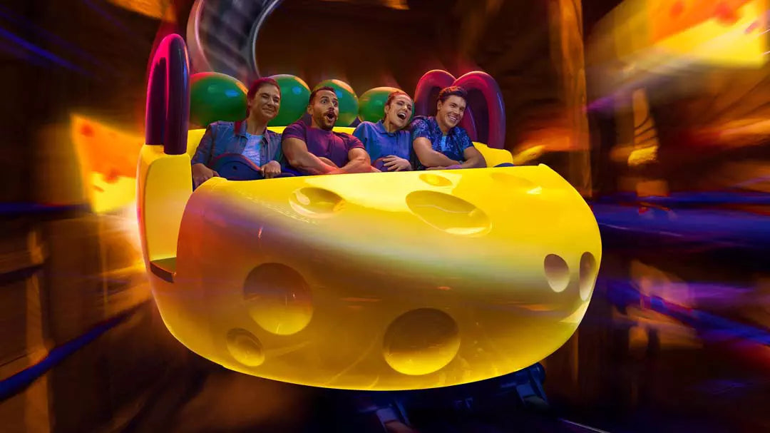 People on a roller coaster ride shaped like a giant cheese wheel with colorful lights in the background.