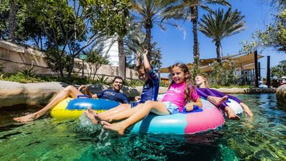 People enjoying inflatable tubes in a pool with palm trees and a clear blue sky.