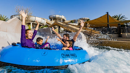 People in a blue tube at a water park with slides and palm trees in the background
