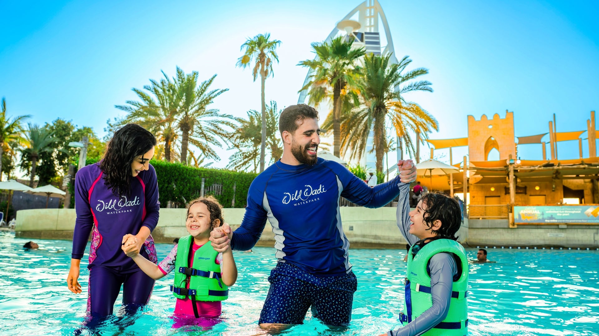 Family with life vests by a pool with palm trees and a building in the background