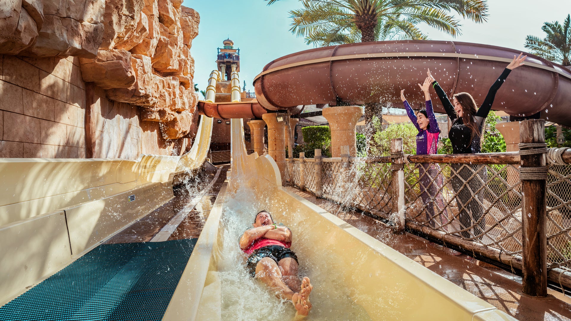 People enjoying a water slide at a water park with palm trees in the background