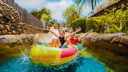 Children on a water slide with a colorful inner tube in a Dubai waterpark setting.