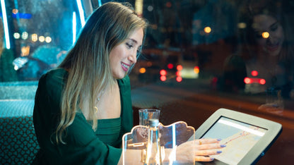 Woman using a tablet in a restaurant with a blurred cityscape background