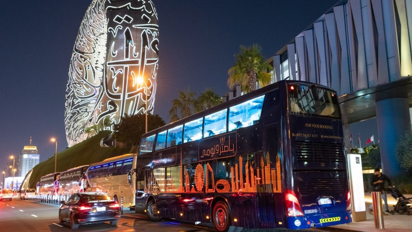 Double-decker bus with illuminated text on a city street at night.