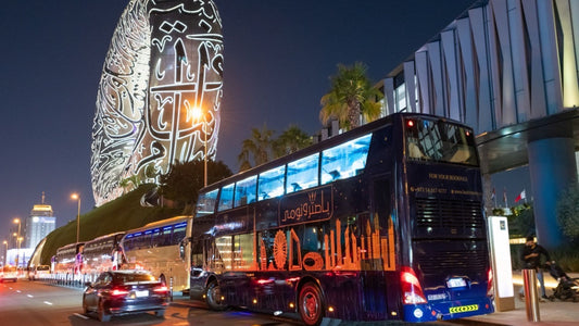 Double-decker bus with illuminated text on a city street at night.