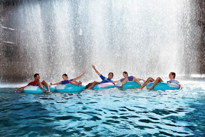 People on inner tubes floating in water with a large waterfall in the background